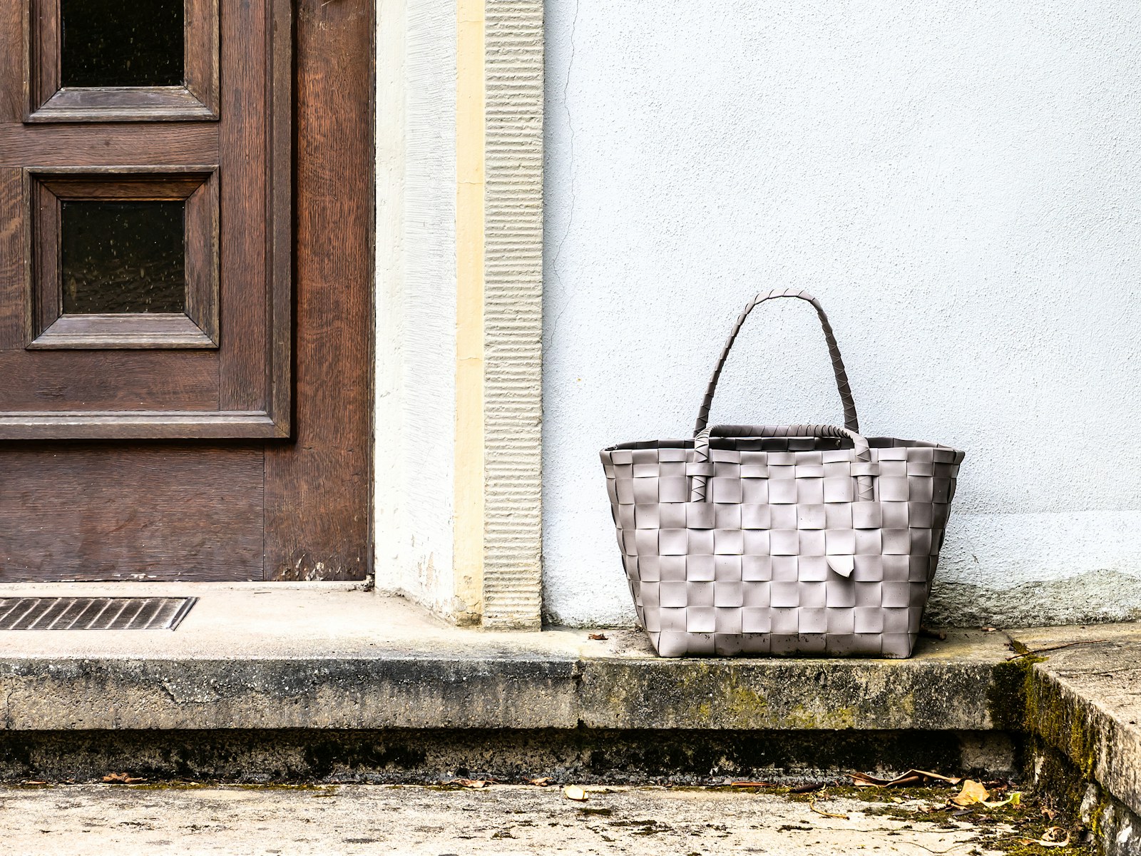 A woven laundry bag resting on the step beside a front door